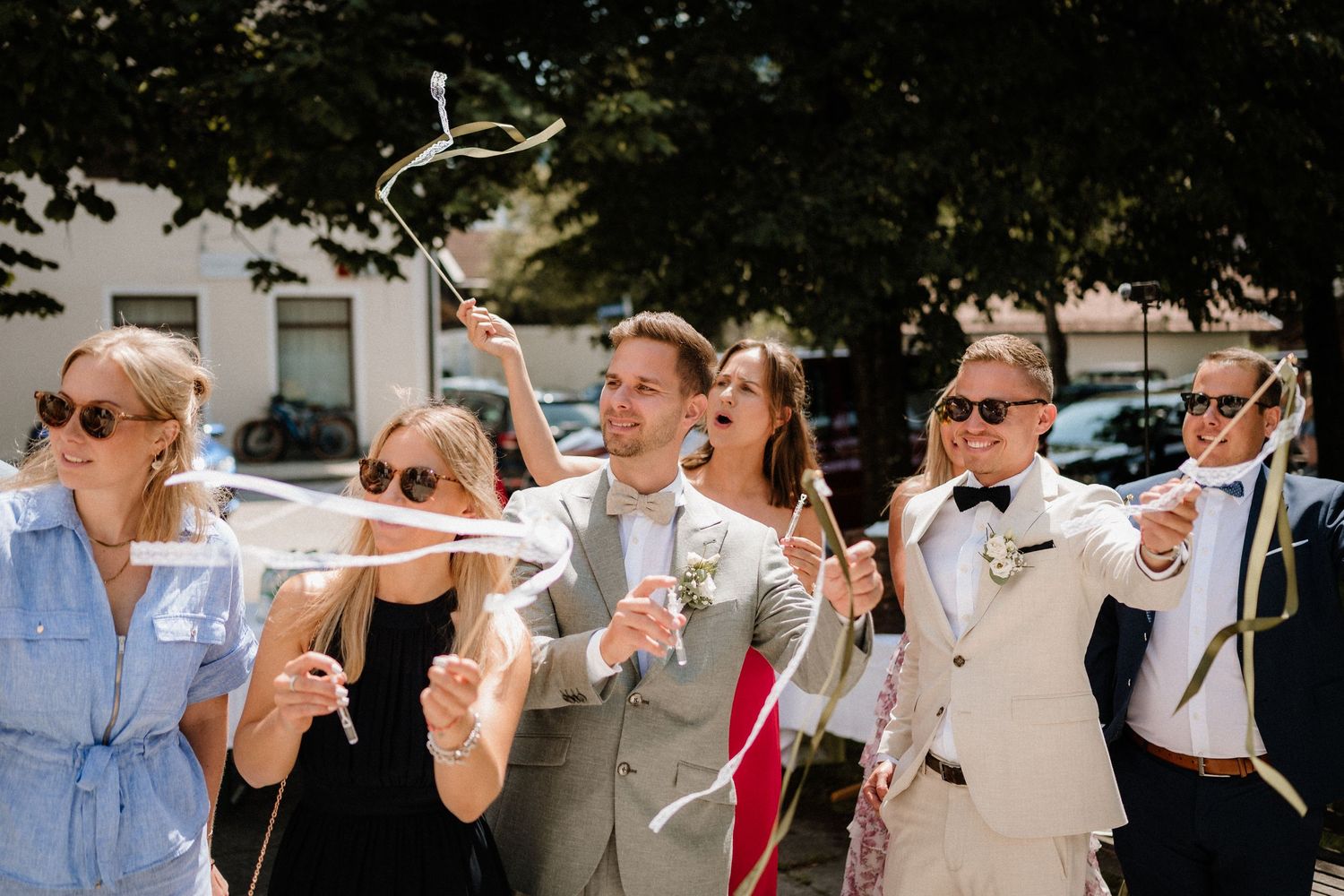 Wedding guests blow bubbles during an outdoor celebration on a sunny day.