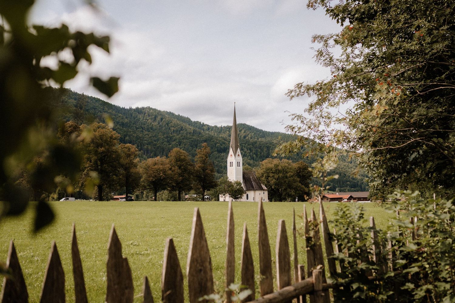 A rustic mountain landscape with wooden fence posts leading to a distant church steeple.