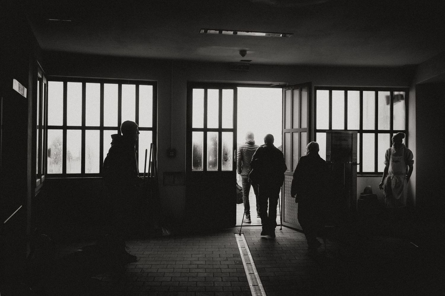 Dark silhouette of people walking through a dimly lit subway station corridor.