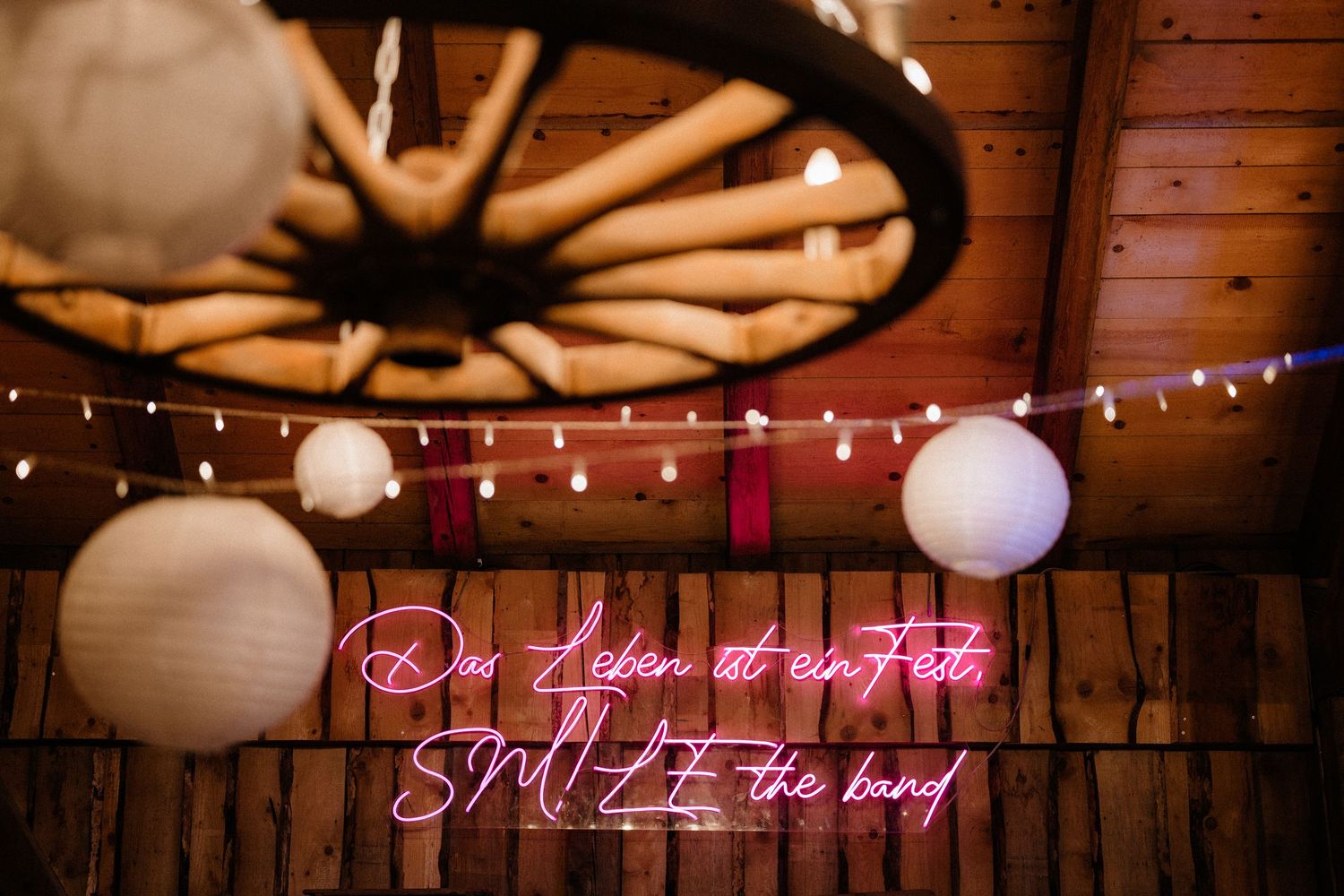 String lights and paper lanterns decorate a rustic wooden barn ceiling creating a romantic ambiance.
