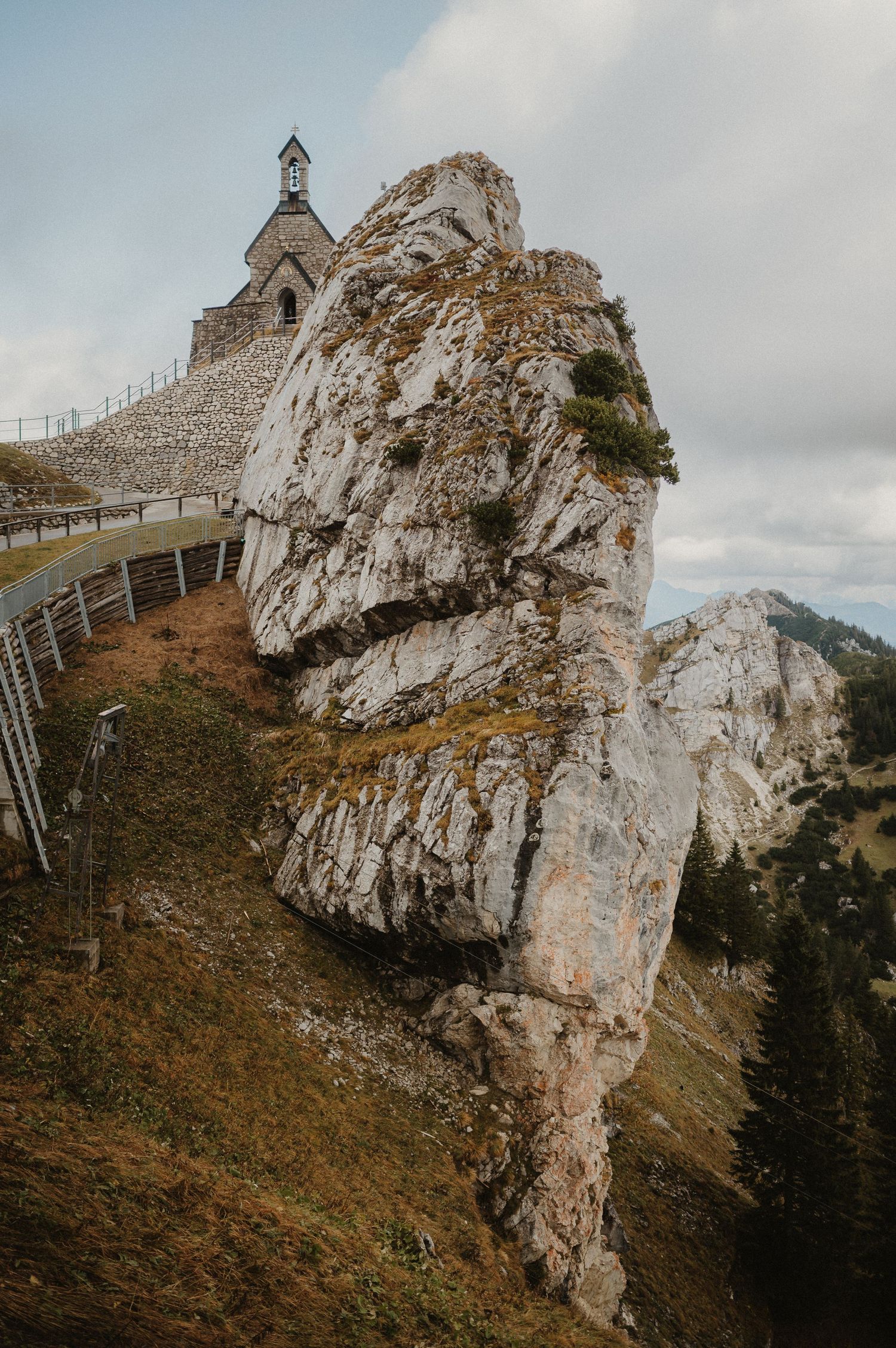 Small chapel perched dramatically on a rocky mountain outcrop with winding path leading to it.