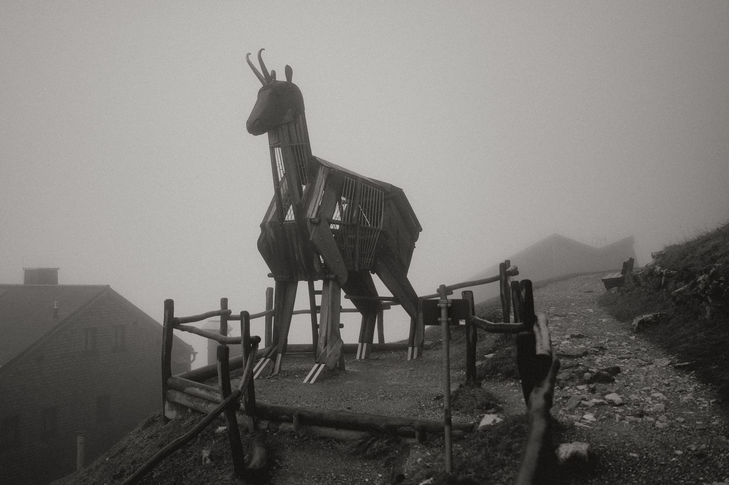 Silhouettes of people walking along a misty mountain ridge with wooden railings.