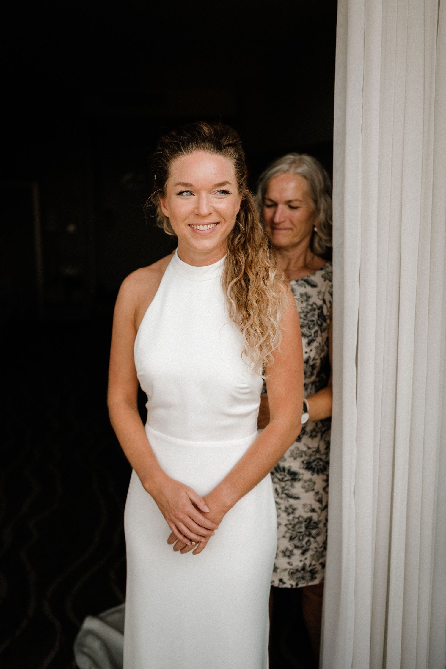 A person in a sleeveless white wedding dress poses against a dark background.