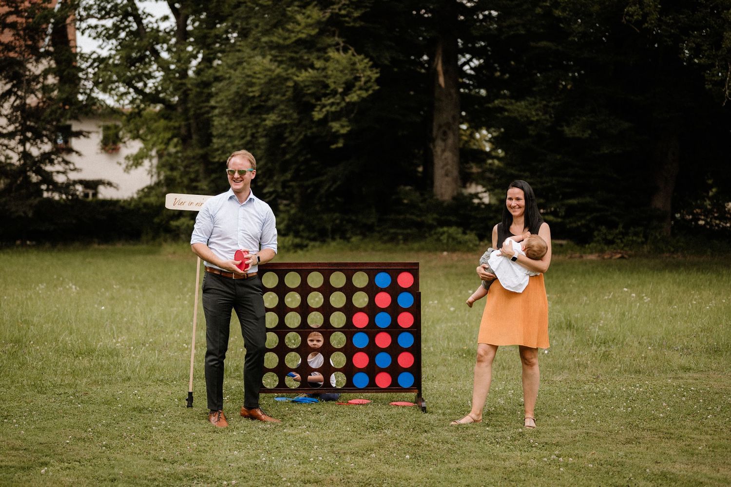 Guests enjoy lawn games at an outdoor wedding reception with a giant Connect Four board.