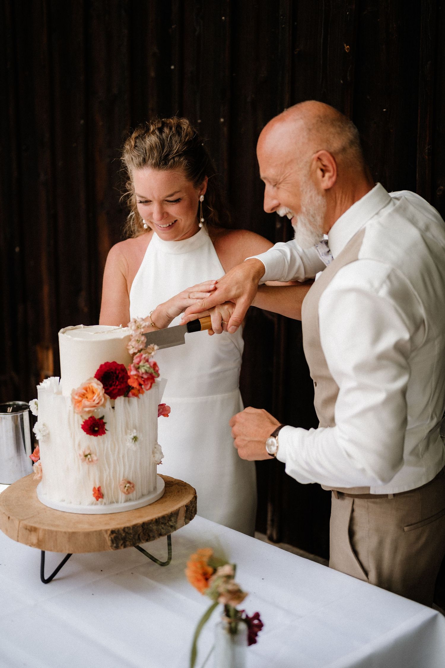 A couple participates in their wedding cake cutting ceremony with a white tiered cake.