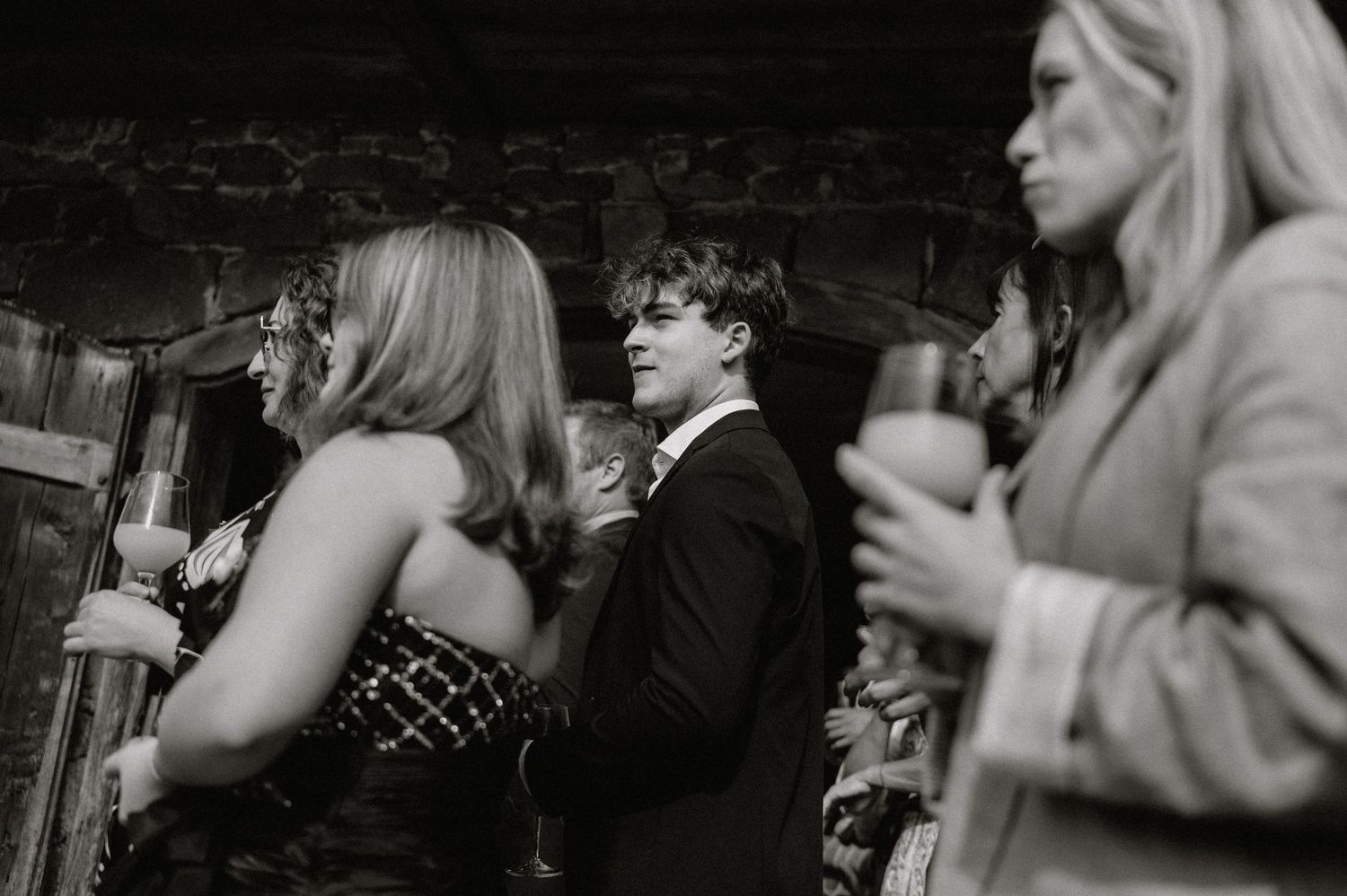 Black and white photo of wedding guests enjoying drinks at a celebration.