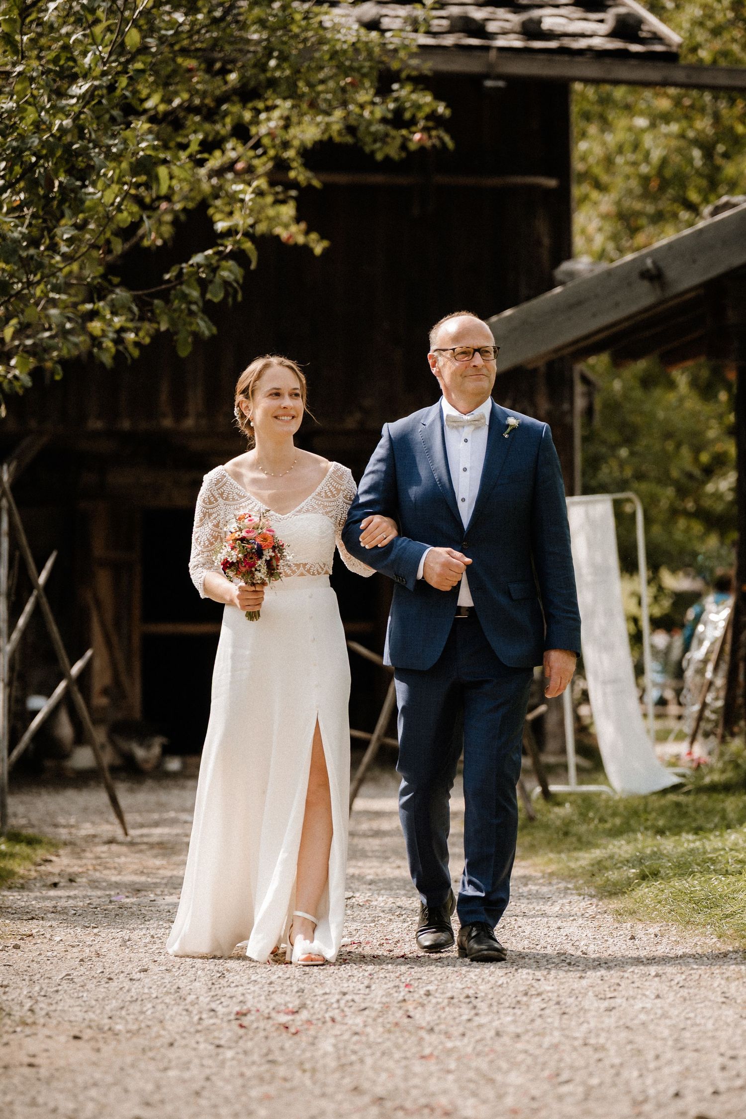Wedding processional on a gravel path near rustic barn.
