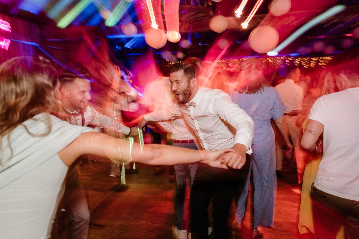 Wedding reception dance floor captured with motion blur and vibrant red and blue lighting effects.
