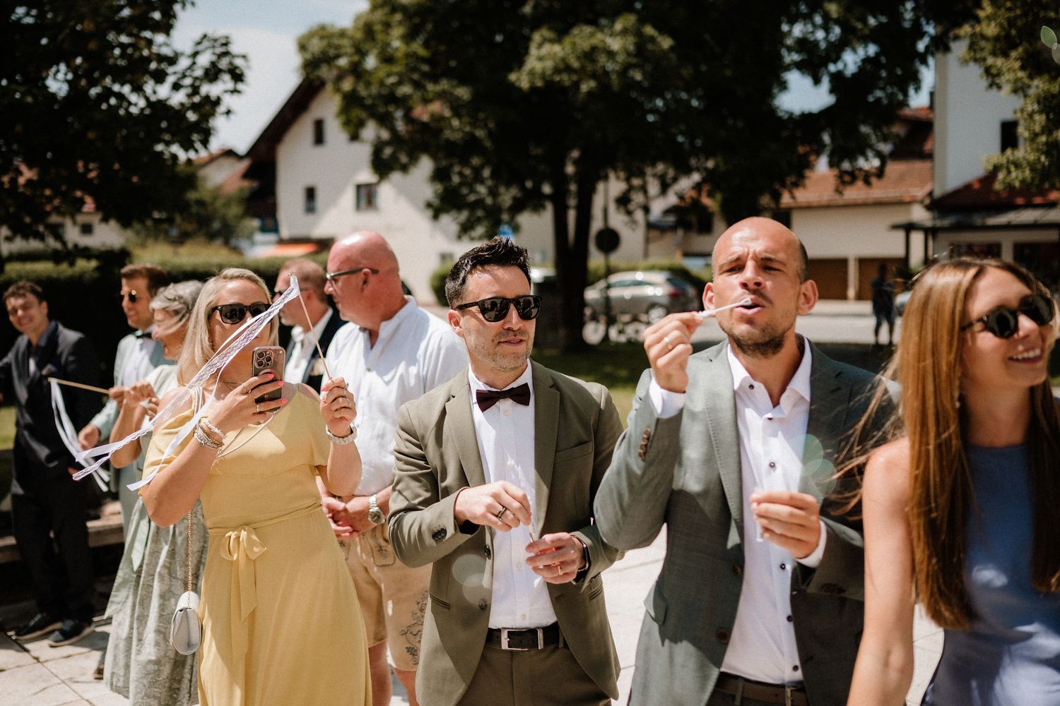 Wedding guests celebrate outdoors with drinks and sunglasses on a bright summer day.