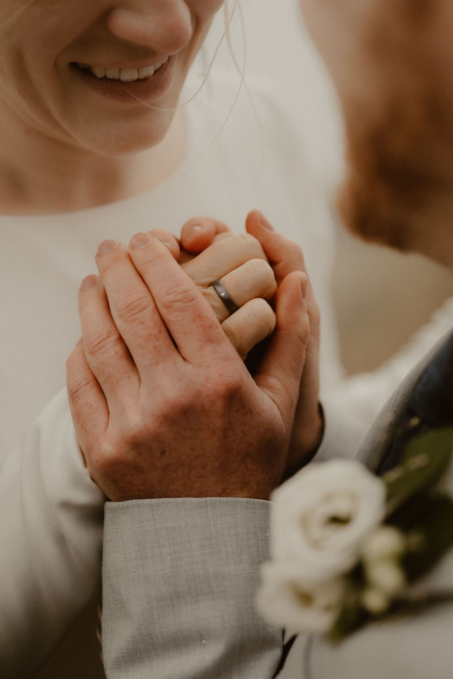 Close-up of hands clasped together with wedding rings and floral details.