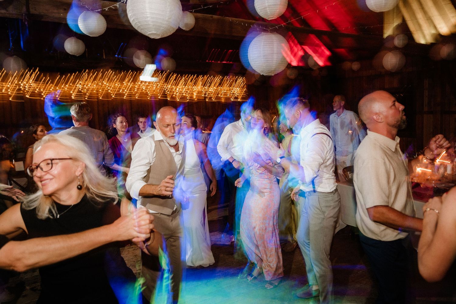 Party guests dancing under white paper lanterns with blue and red lighting effects.