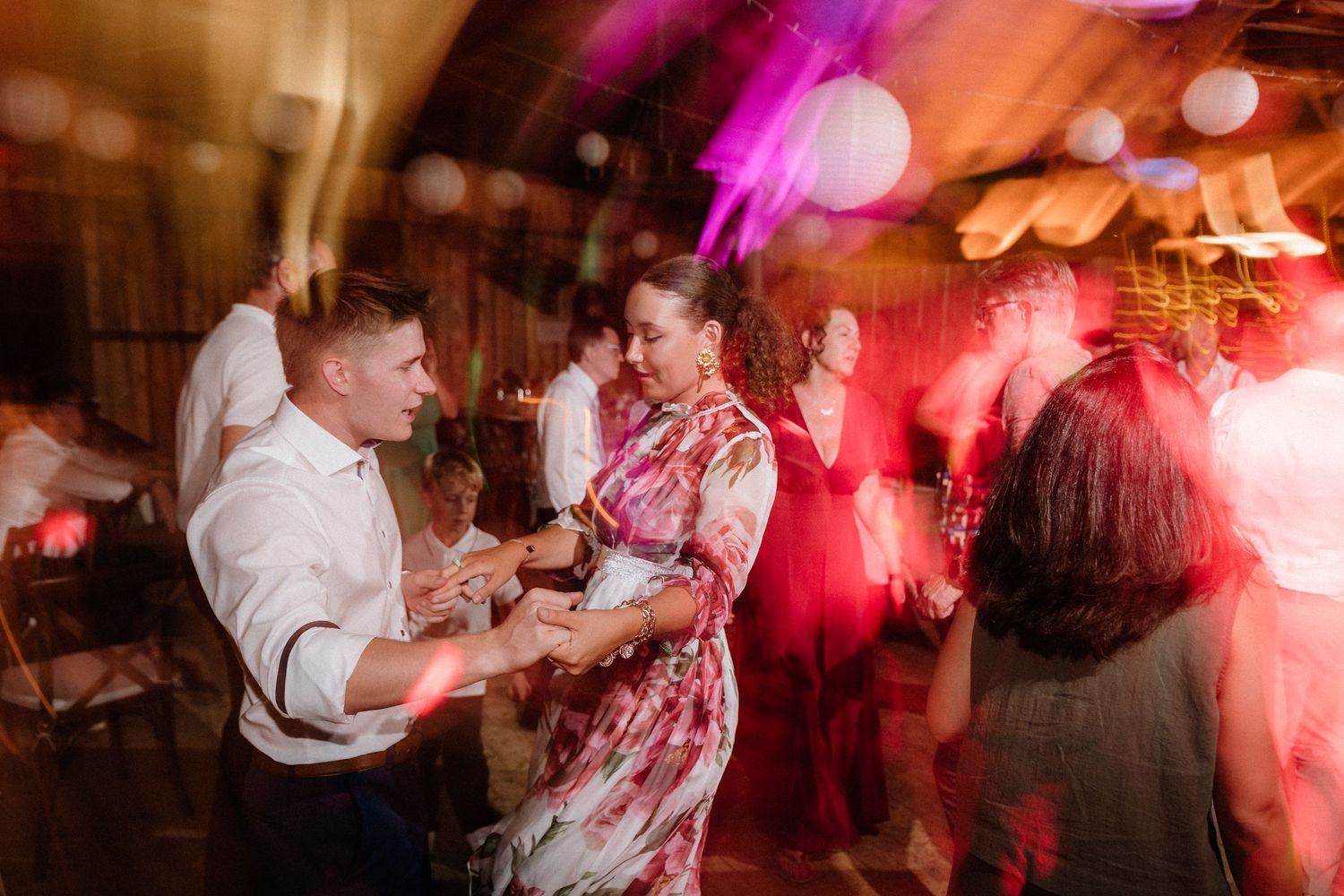 Wedding reception dance floor filled with guests dancing under vibrant pink and red lighting effects.