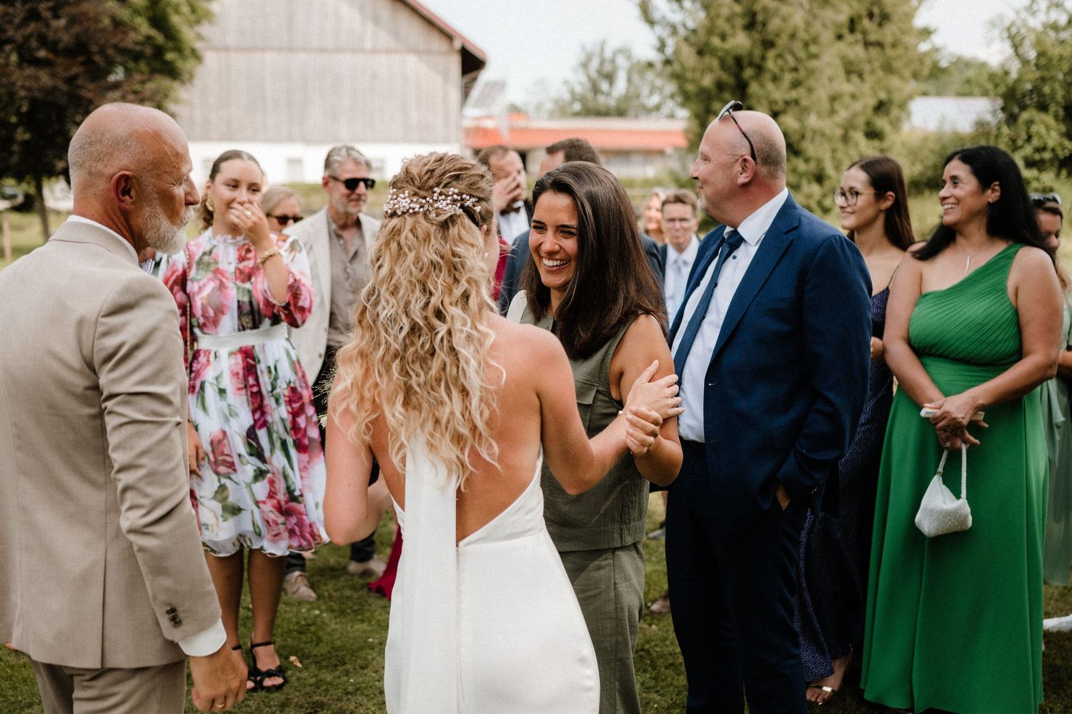 Wedding celebration on a lawn with guests in formal wear and bright dresses.