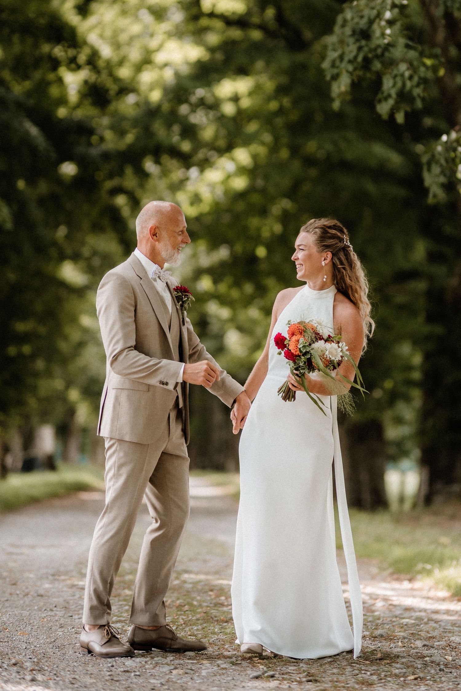 Candid wedding photography captures couple's laughter and joy on a sunlit forest path.