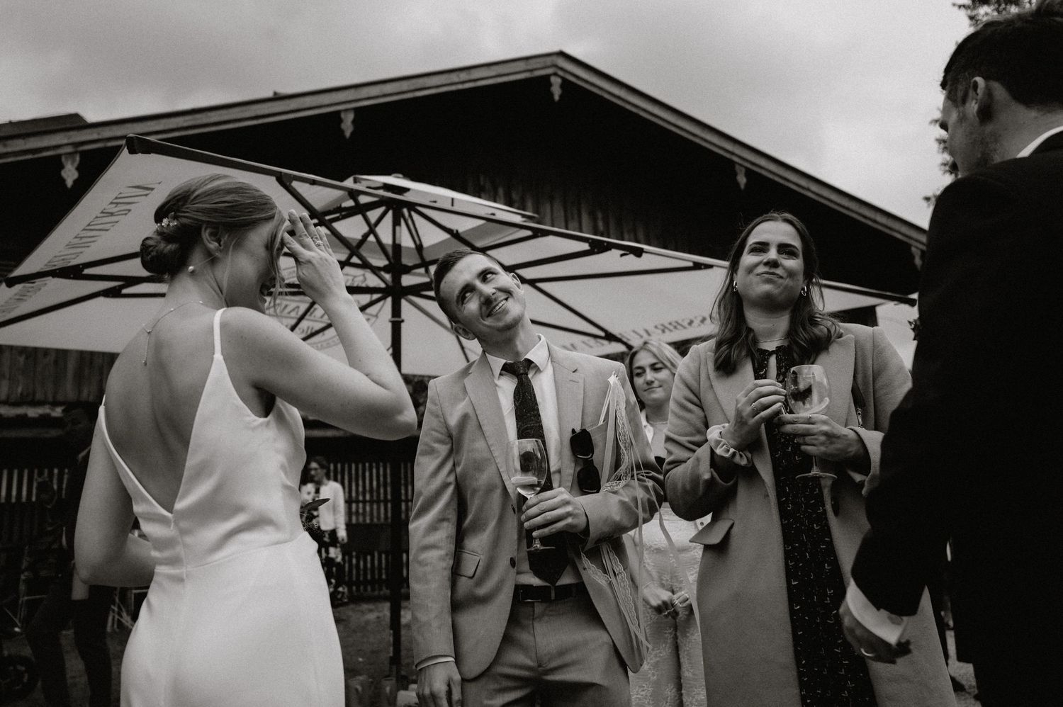 Wedding celebration under white umbrellas outside rustic wooden buildings.