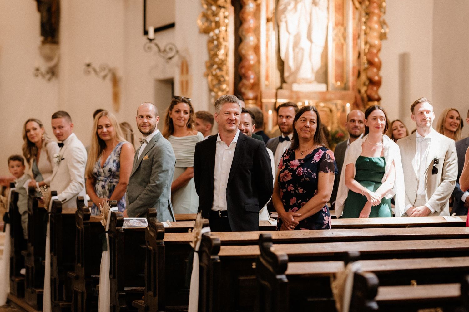 Wide shot of wedding guests seated in wooden pews during church ceremony.