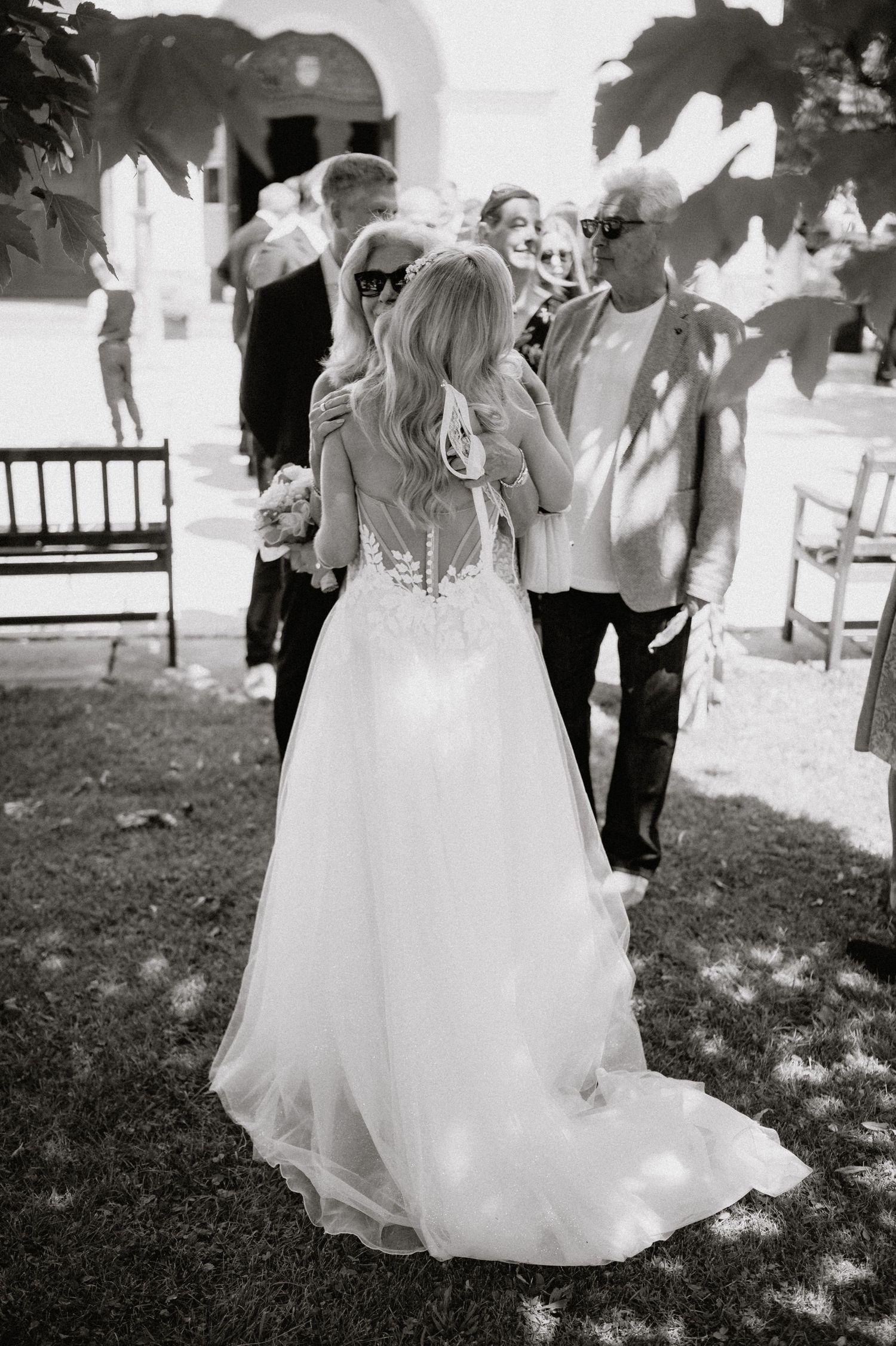 A black and white photo of a bride in a flowing white dress at an outdoor garden wedding.