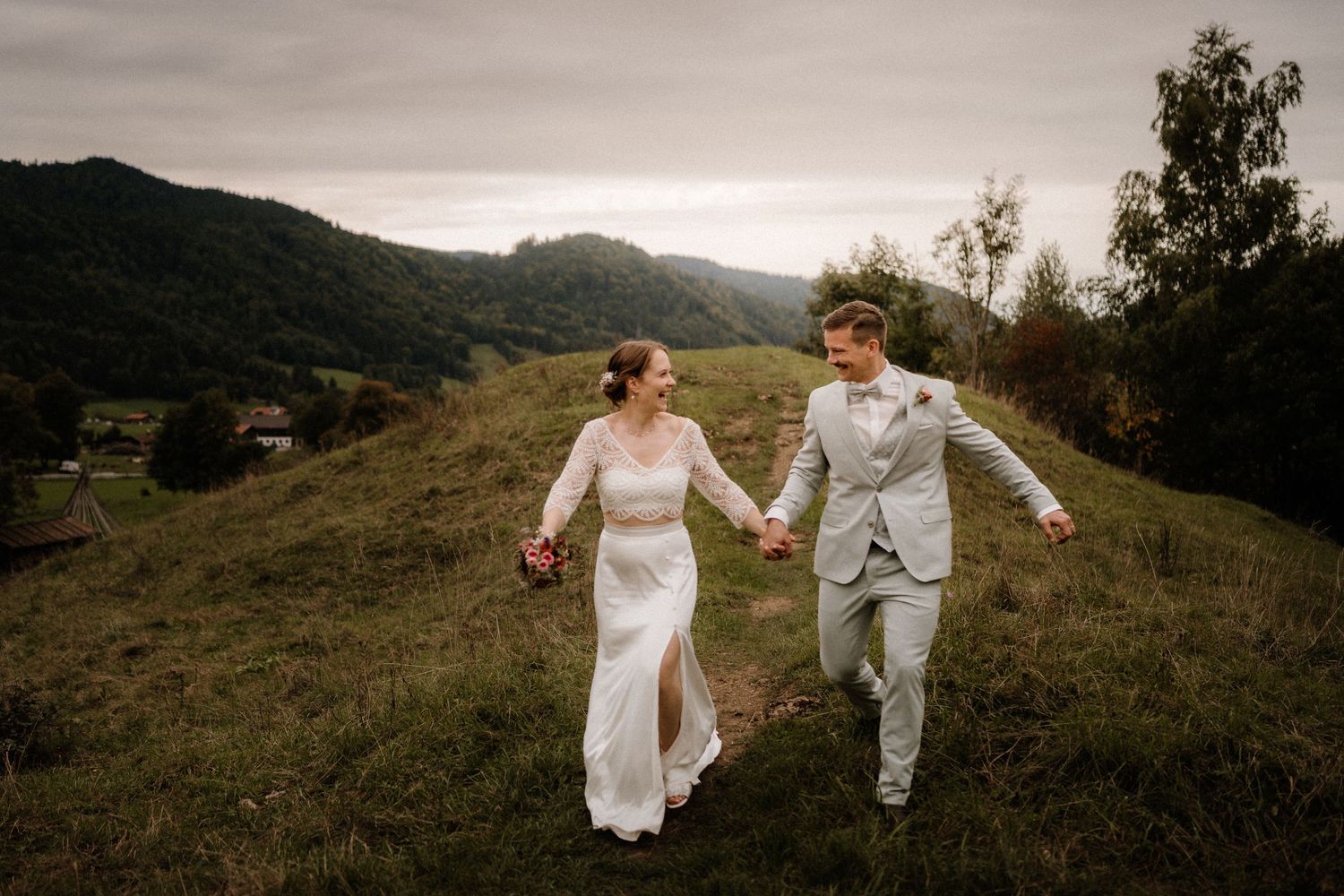 Wedding couple traverses scenic mountain terrain with dramatic cloudy backdrop.