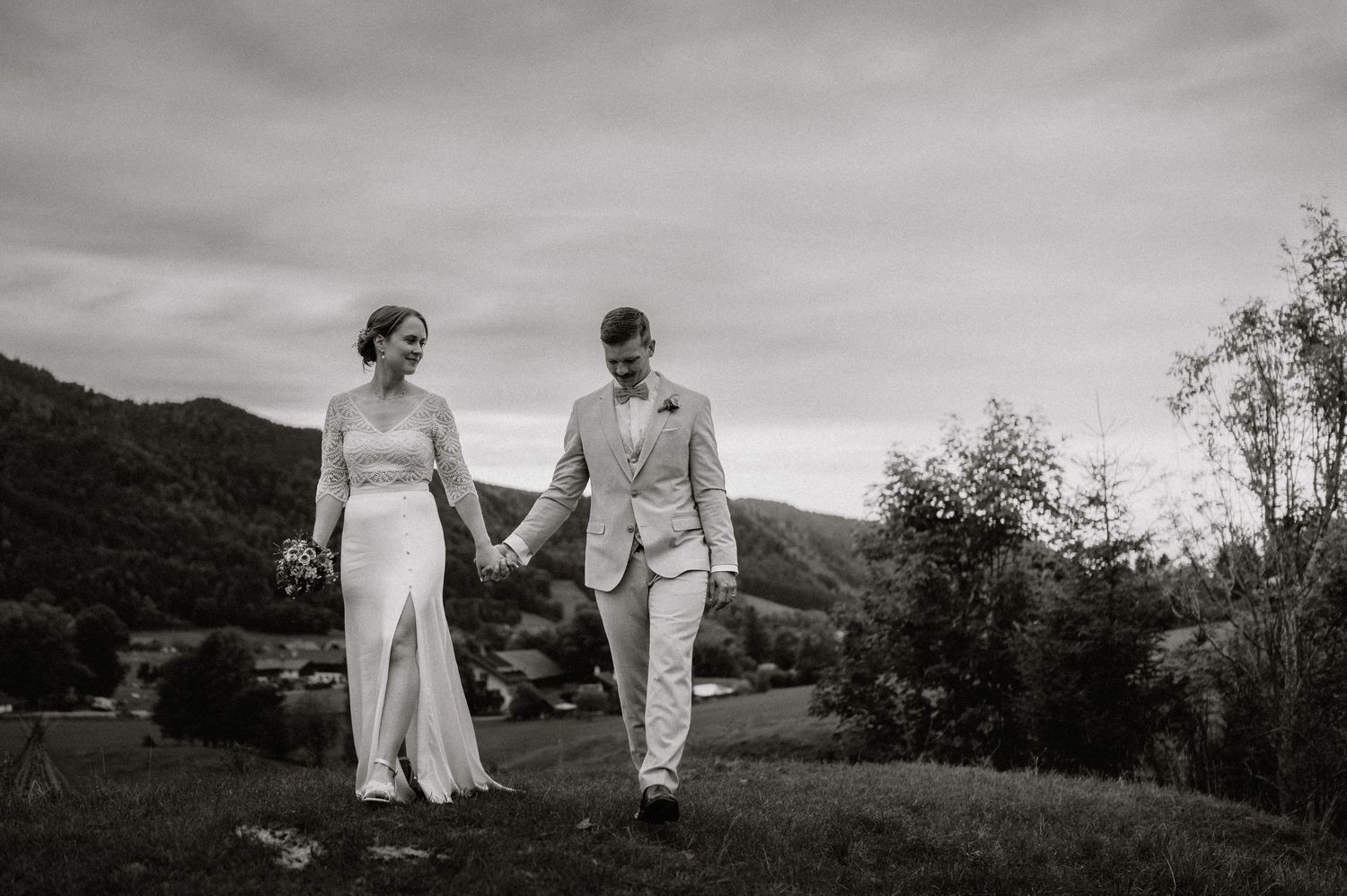 Couple in wedding attire walking through mountain meadow in dramatic black and white.
