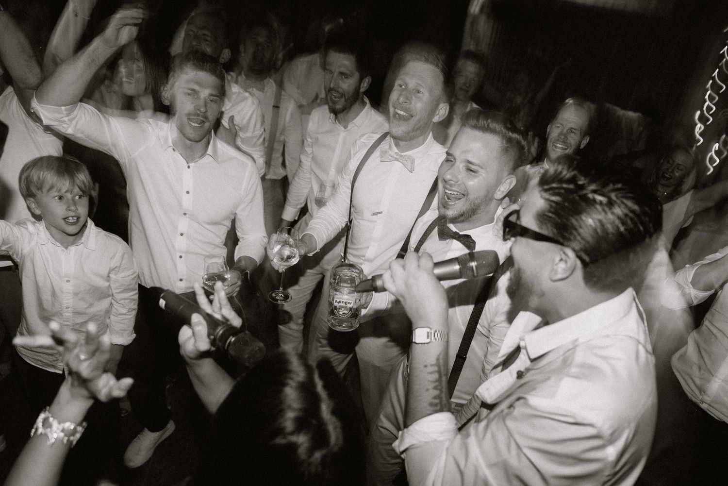 A lively black and white photo of guests laughing and celebrating at a wedding reception.