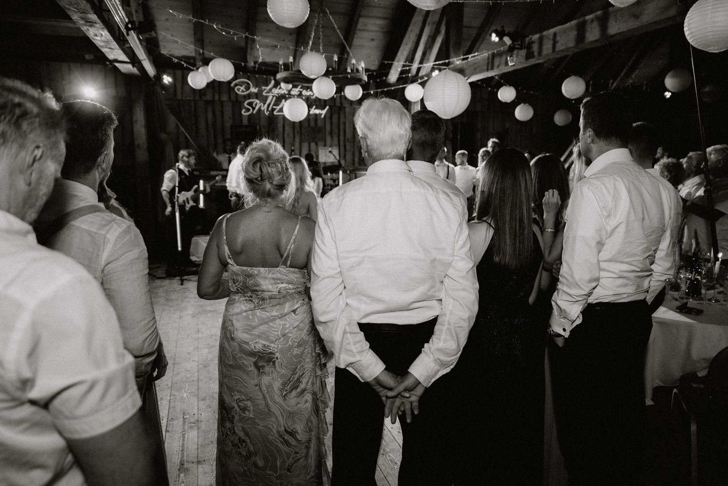 Black and white shot of wedding guests dancing under paper lanterns at a reception.