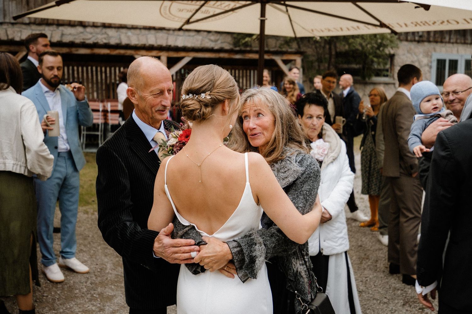 Wedding guests share joyful hugs with the bride at an outdoor reception under a tent.
