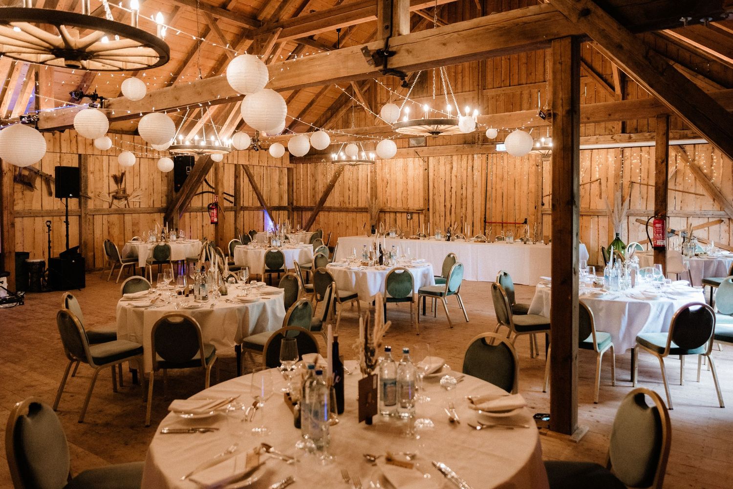 A rustic barn wedding reception venue with wooden beams and hanging lights.