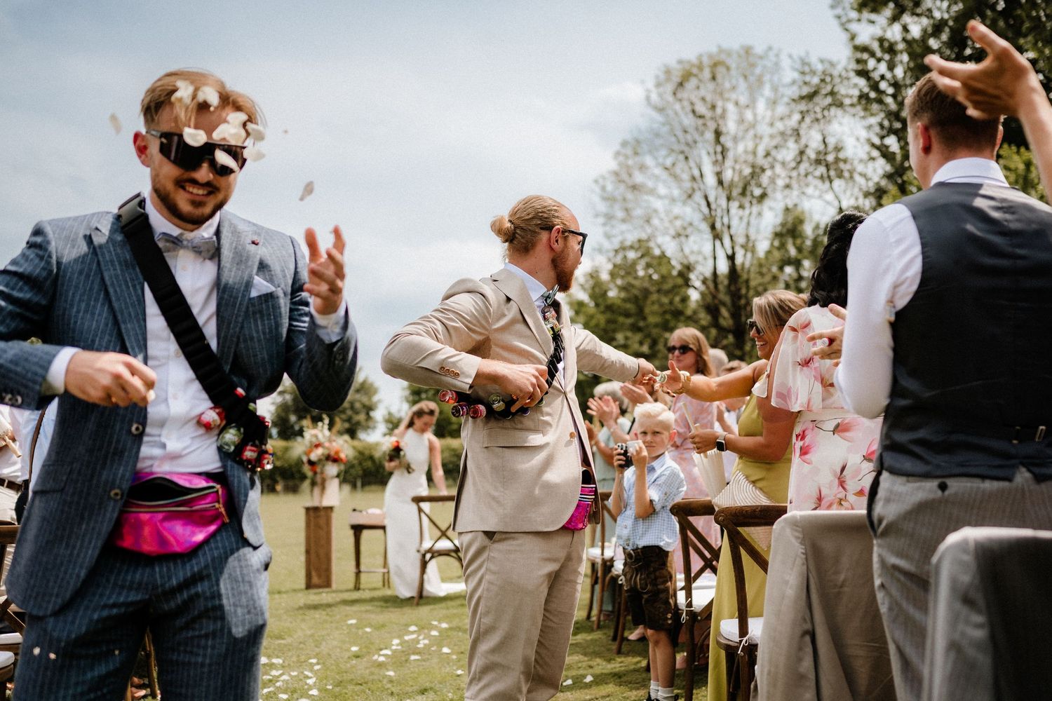 Wedding guests seated in wooden chairs during an outdoor ceremony with floral decorations.