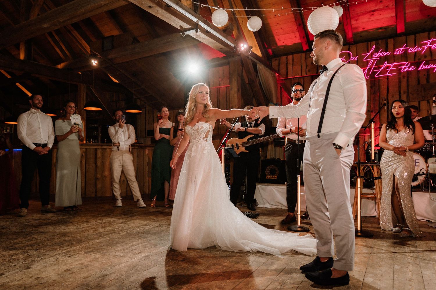 Wedding celebration in a barn with red ambient lighting and white paper lanterns hanging from ceiling.