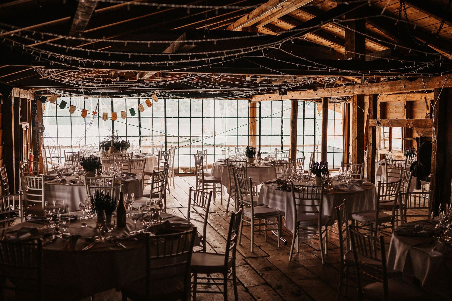 A rustic wooden barn interior with exposed beams, windows, and scattered chairs creates a warm, vintage atmosphere.