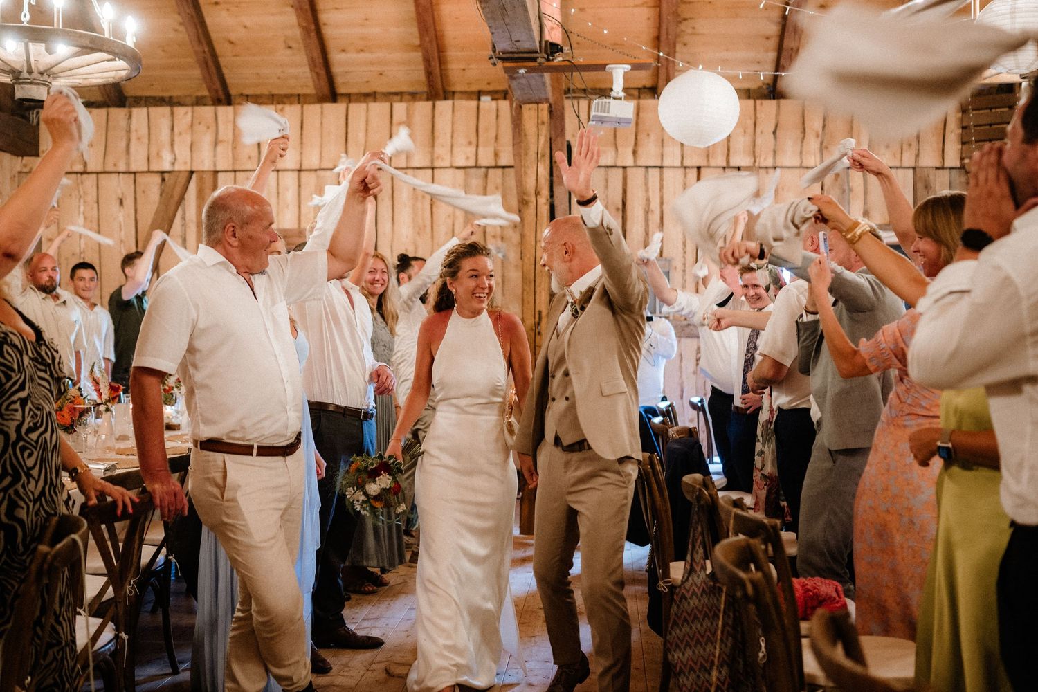 Energetic wedding reception scene with guests dancing and celebrating in a rustic barn setting.