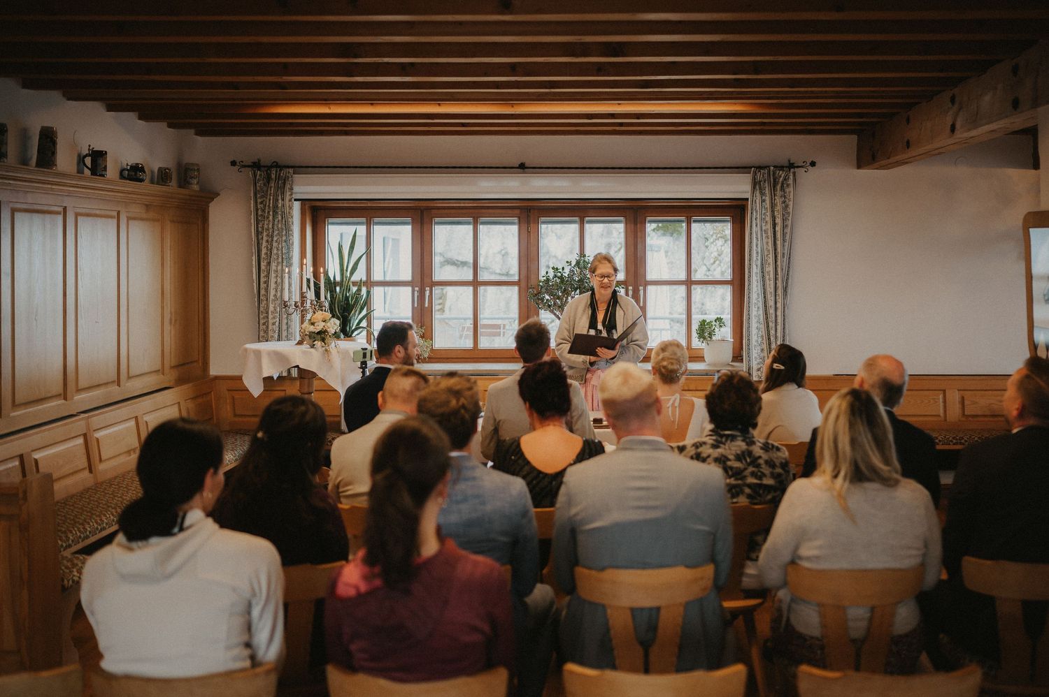 Guests seated in rows at an indoor wedding ceremony with wooden beams and natural lighting.