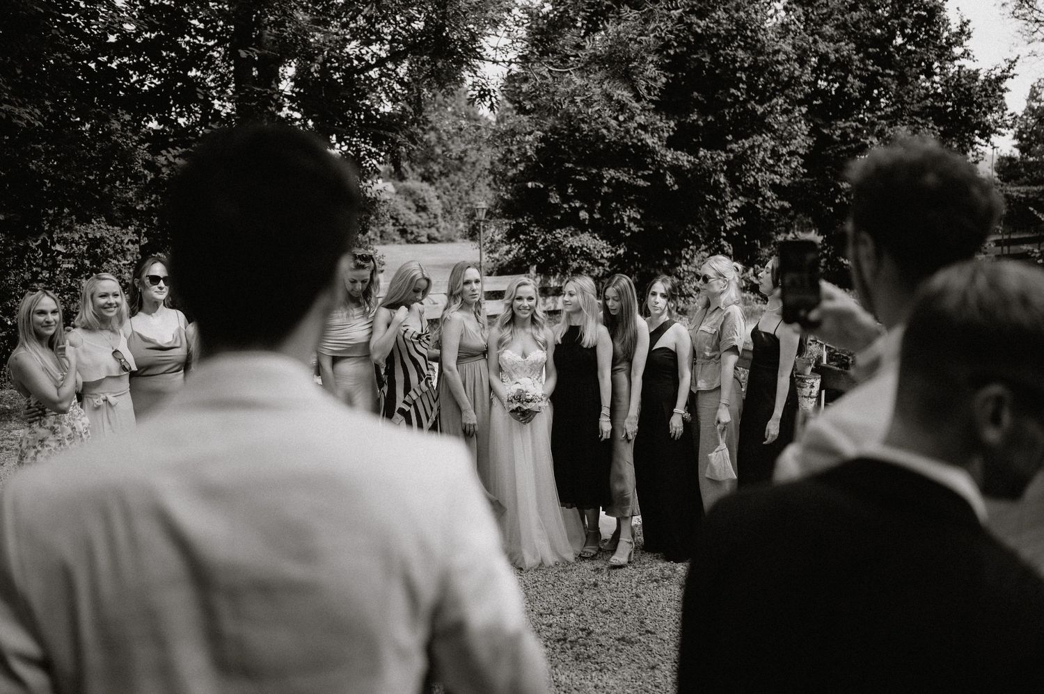 Wedding ceremony guests gathered outdoors for group photos in black and white.