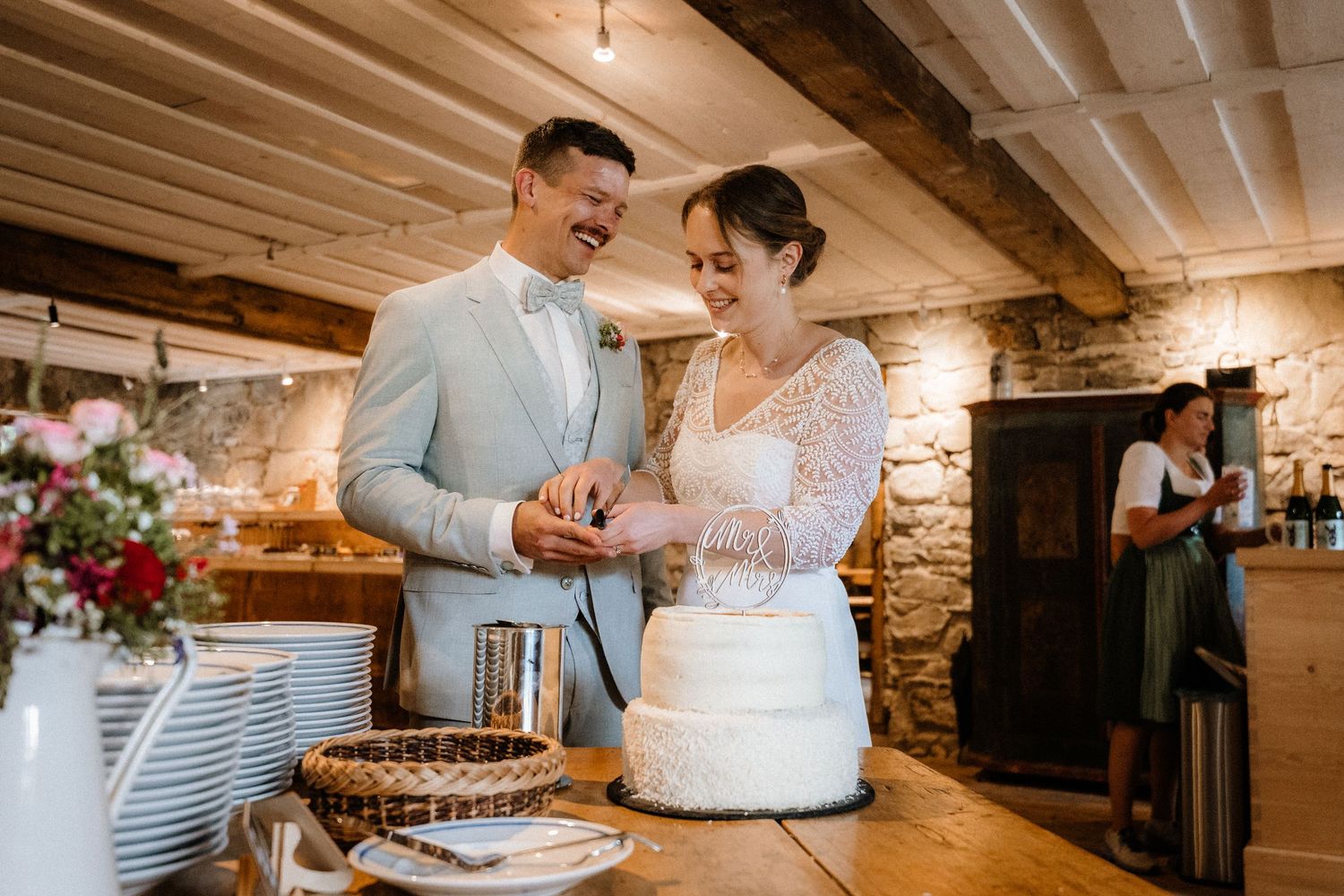 Wedding reception setup in rustic venue with white cake and floral arrangements.