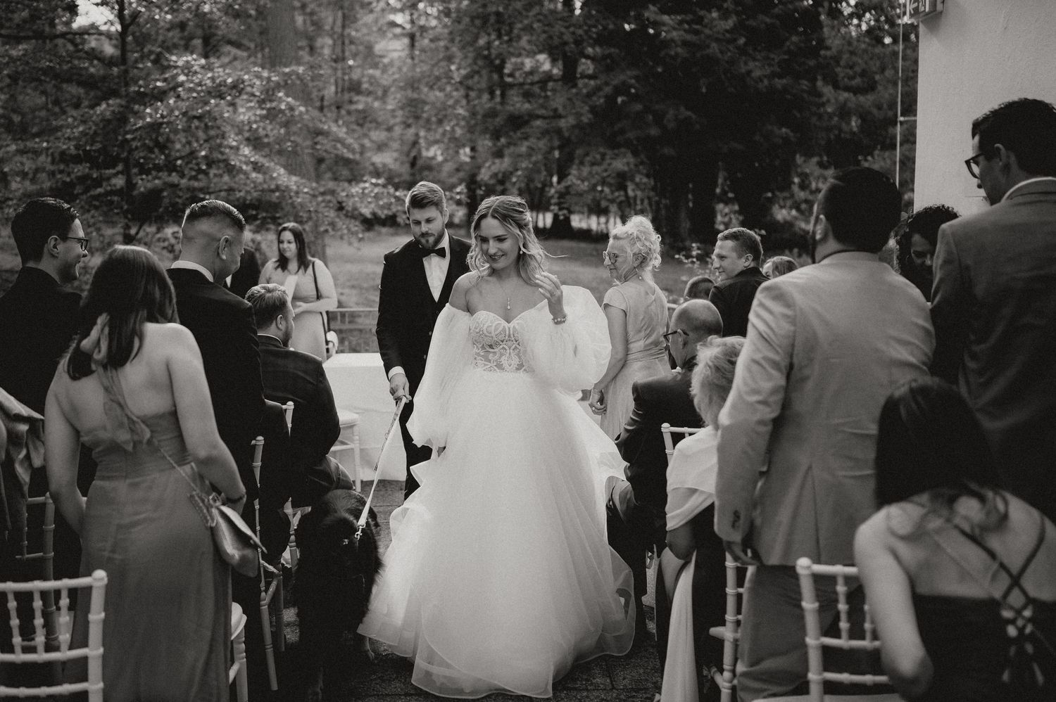 A panoramic view of wedding guests seated at an outdoor ceremony with white chairs.
