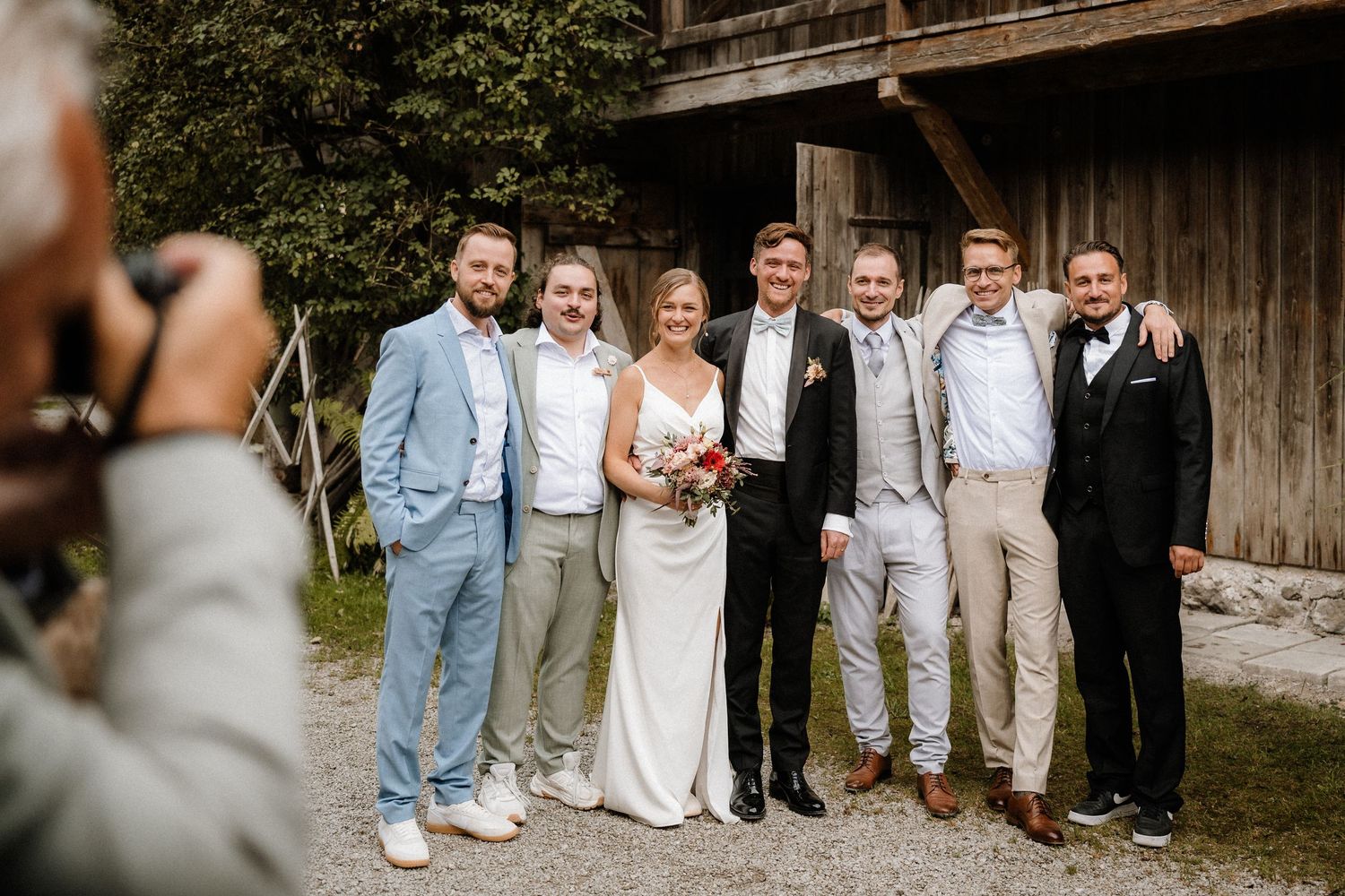 Wedding party lined up against weathered barn wall for formal group portraits.