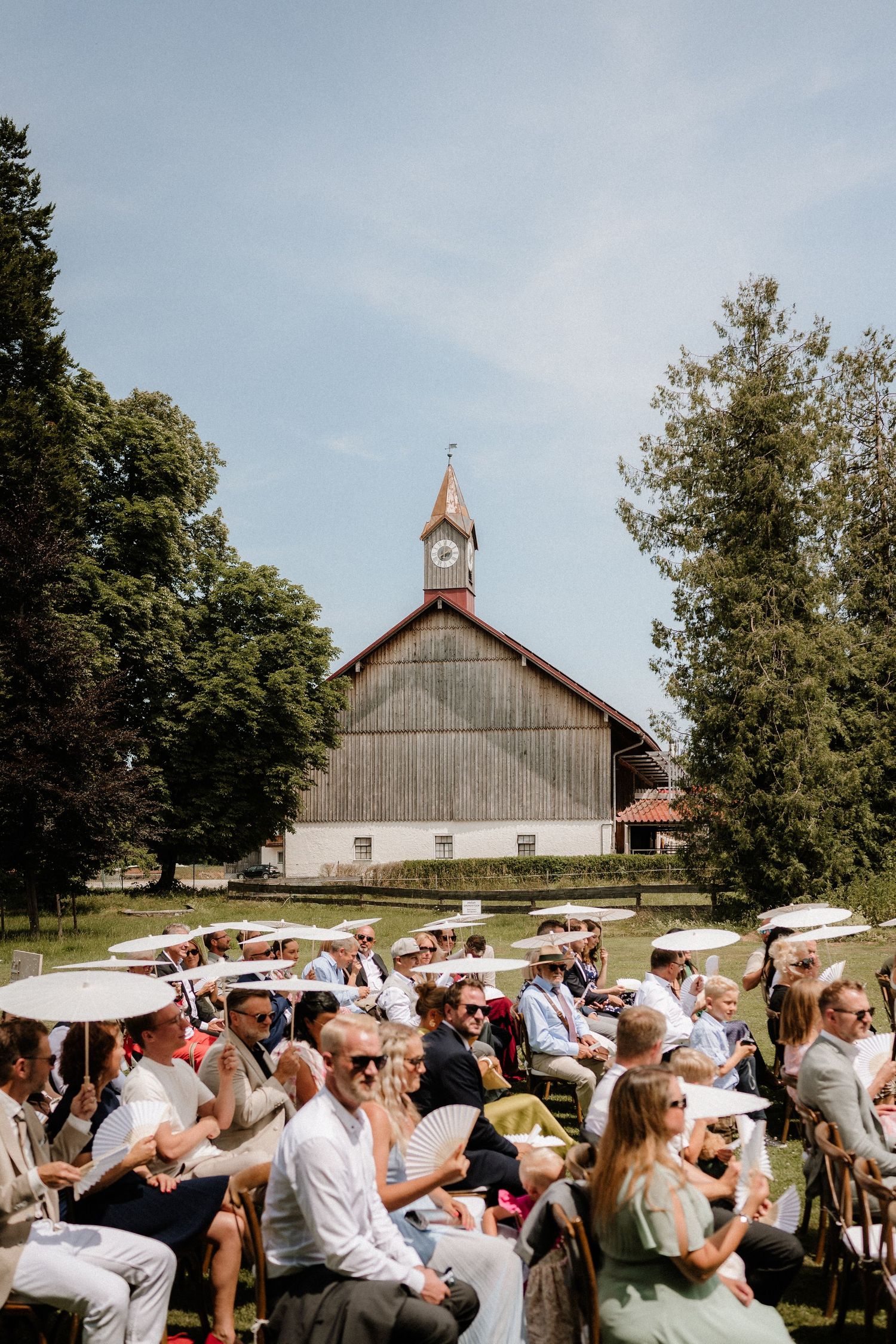 Rustic barn wedding venue with guests shading themselves under a bright summer sky.