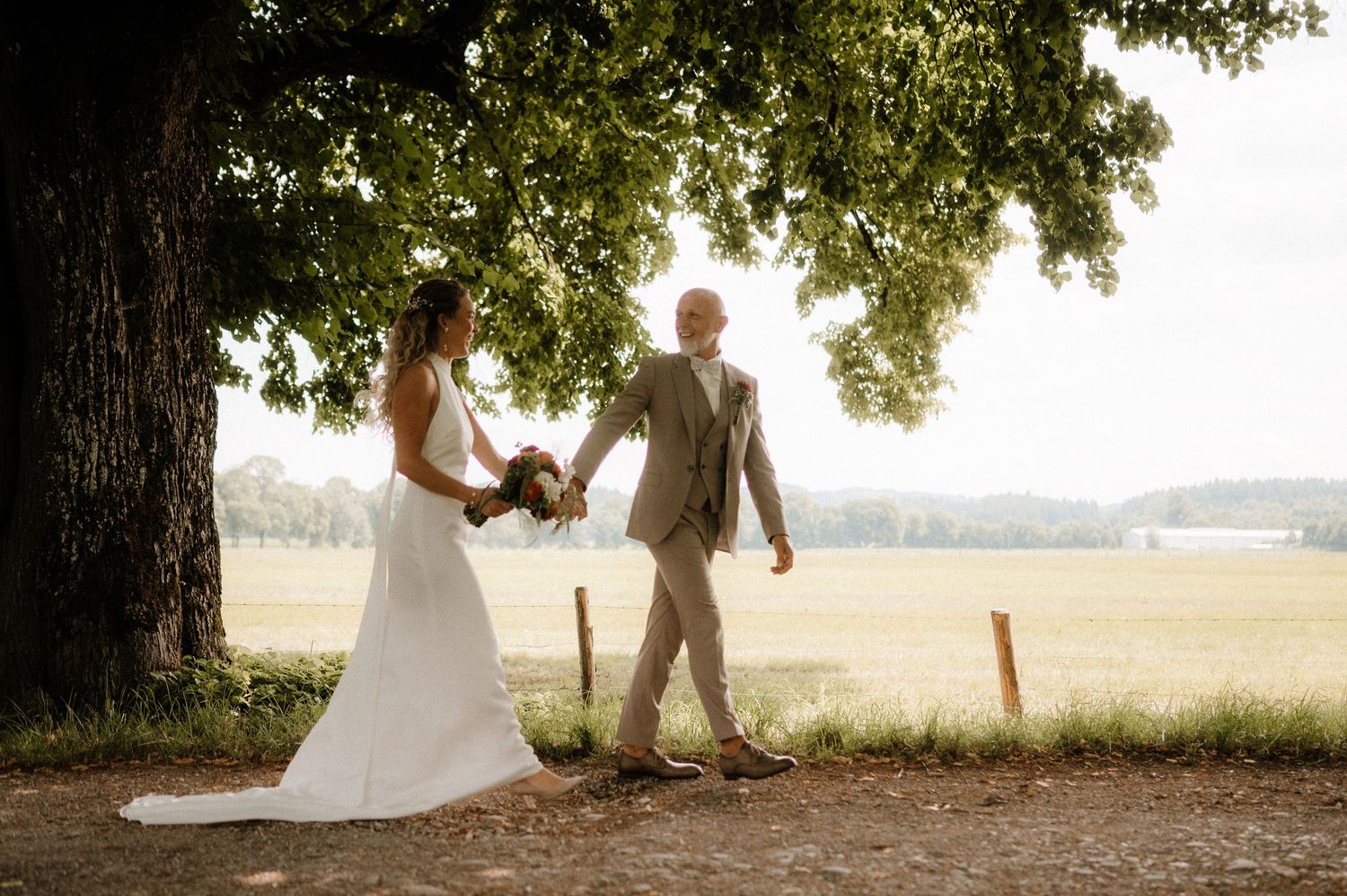A wedding couple shares an intimate moment under large trees in a natural outdoor setting.