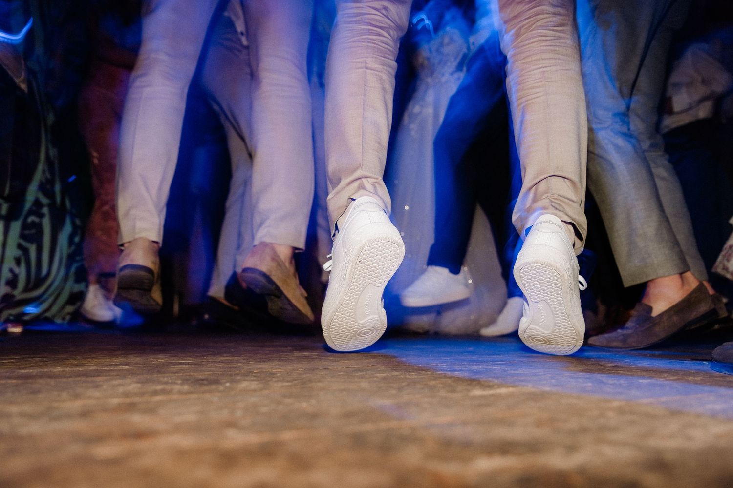 Dance floor filled with people's feet in white socks and shoes under blue lighting at a party.