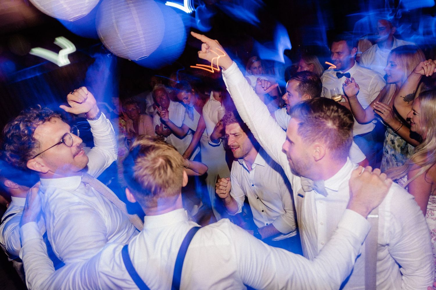 Energetic wedding party dancing and celebrating under blue atmospheric lighting.