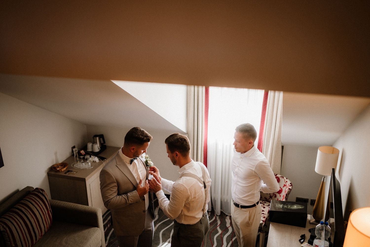 Three people getting ready in a hotel room with warm lighting and casual attire.