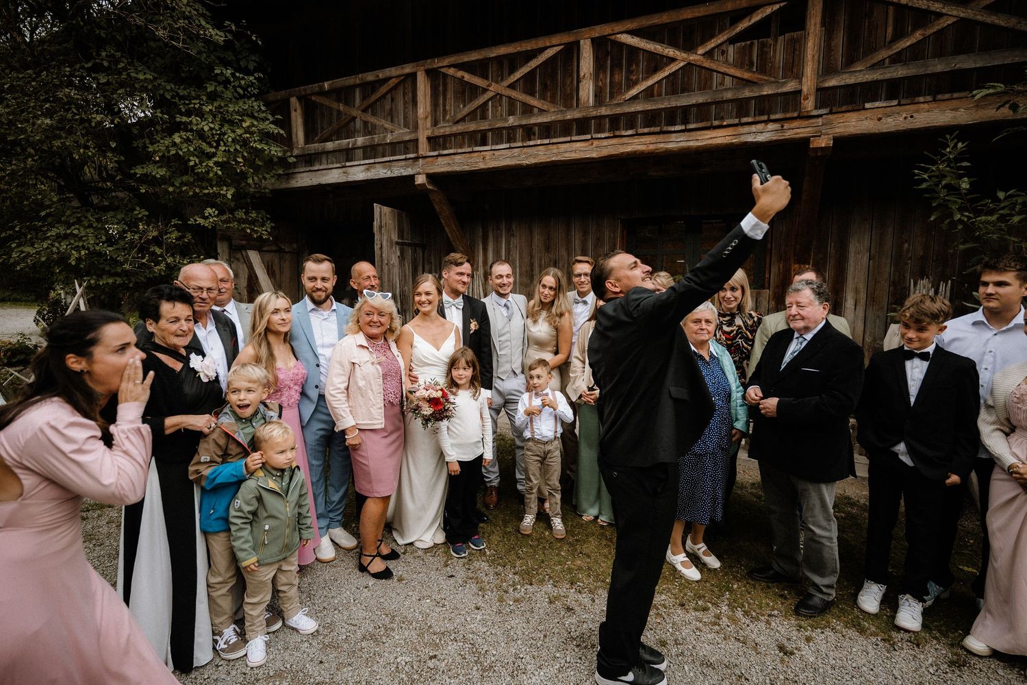 Wedding guests and party members gather outside a rustic wooden barn for celebratory photos.