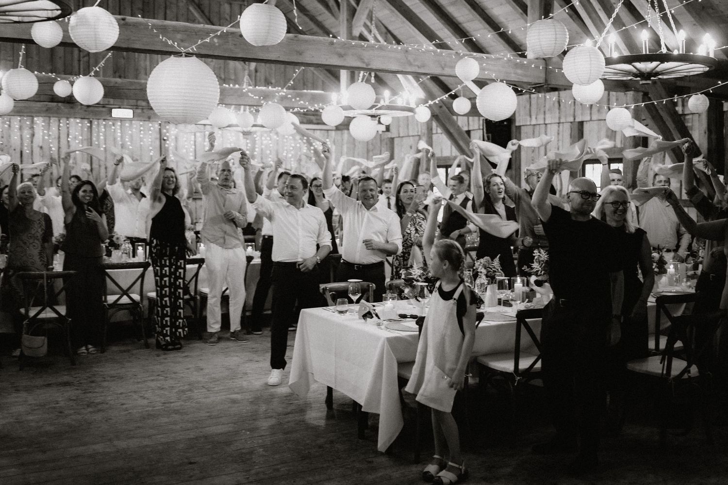 Wedding reception in a barn with paper lanterns and guests mingling around decorated tables.