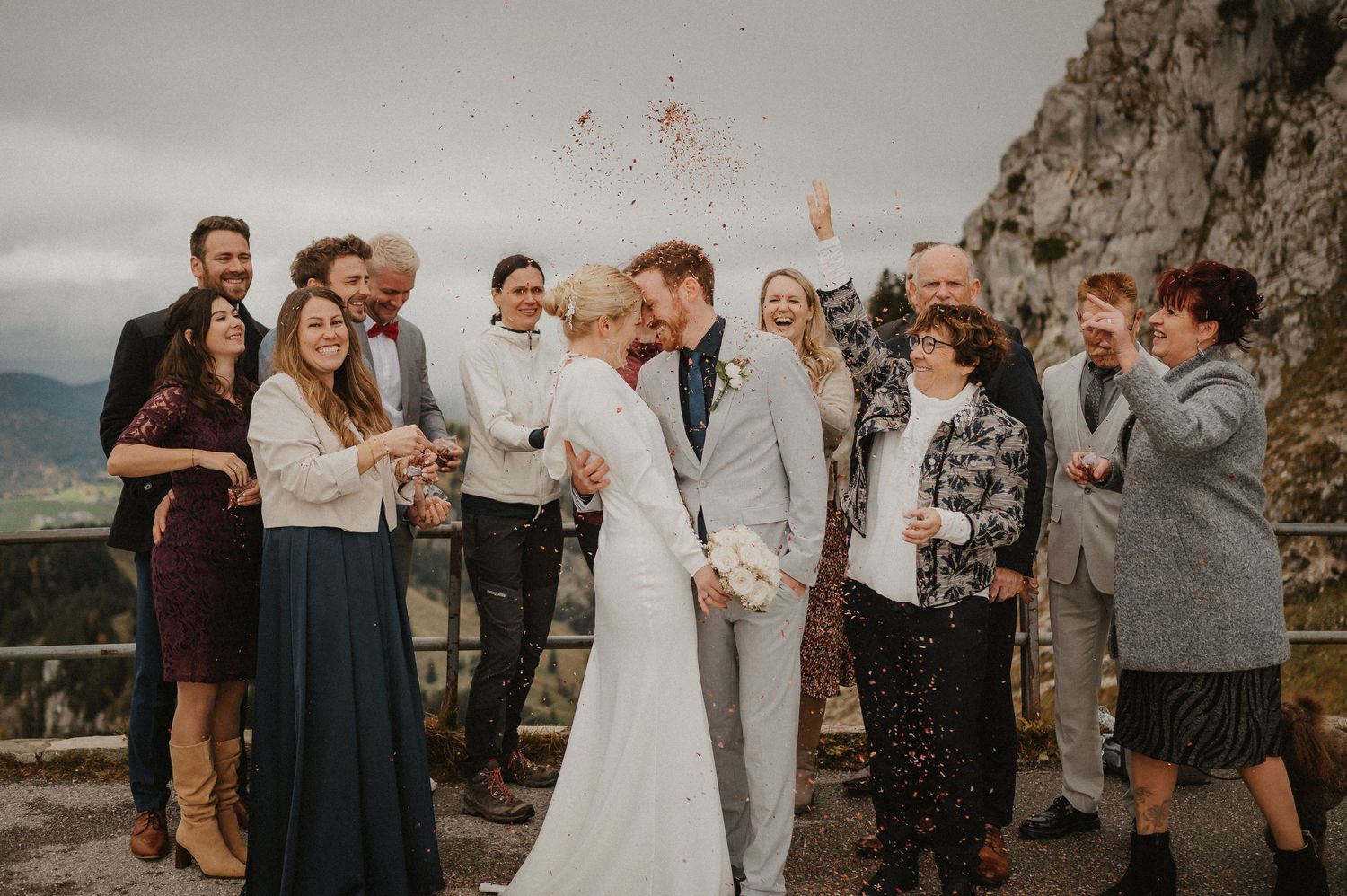 Wedding party celebrating with confetti against dramatic mountain backdrop.
