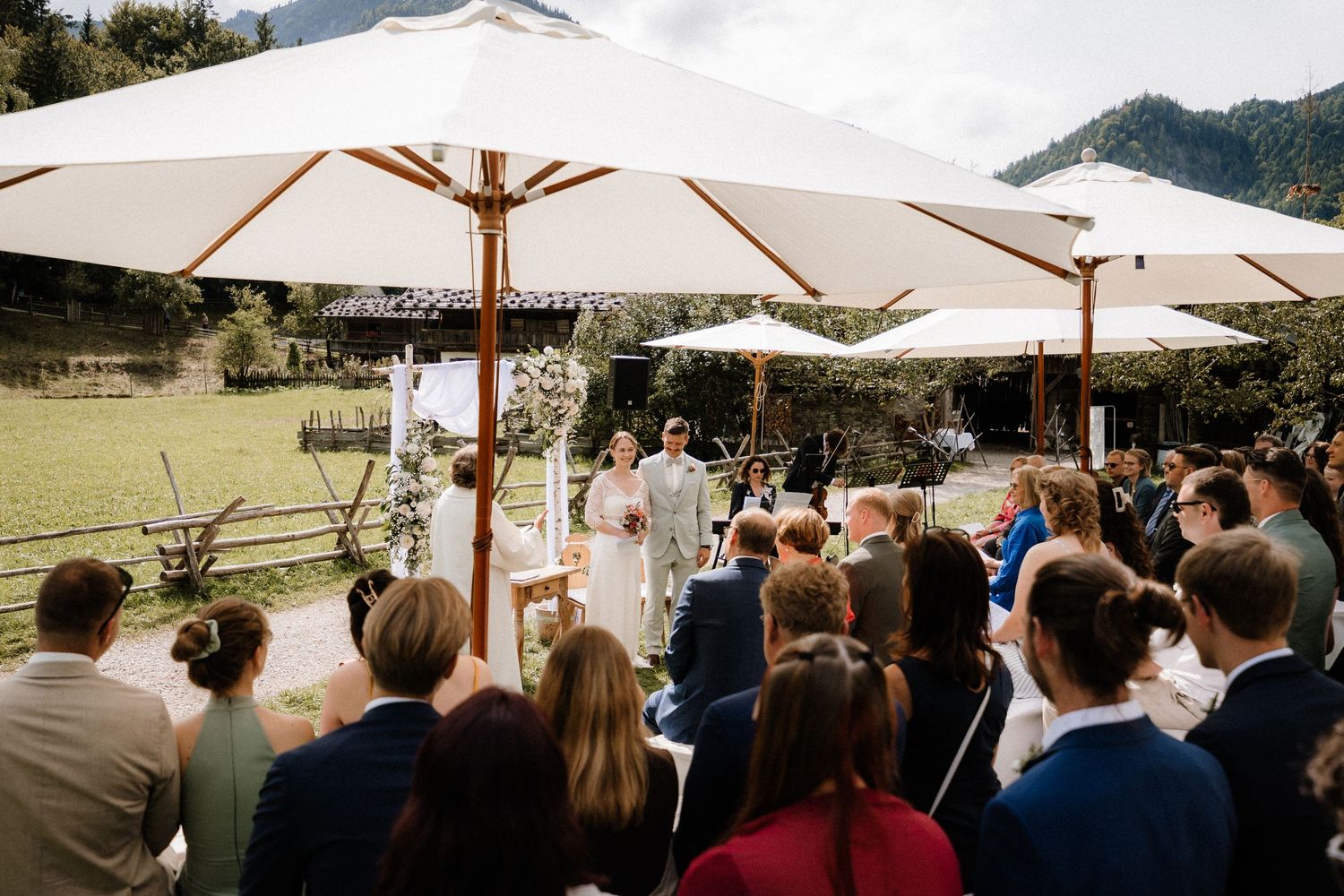 Outdoor wedding ceremony under white umbrellas with mountain backdrop.