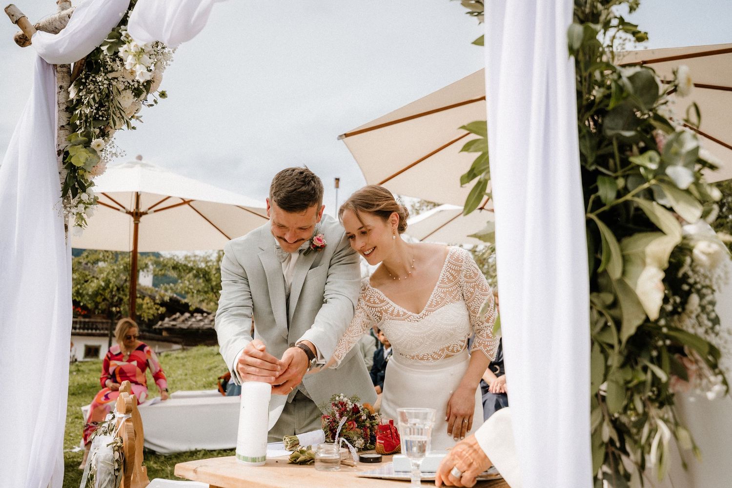 An outdoor wedding ceremony setup with white drapes and floral decorations against a natural backdrop.