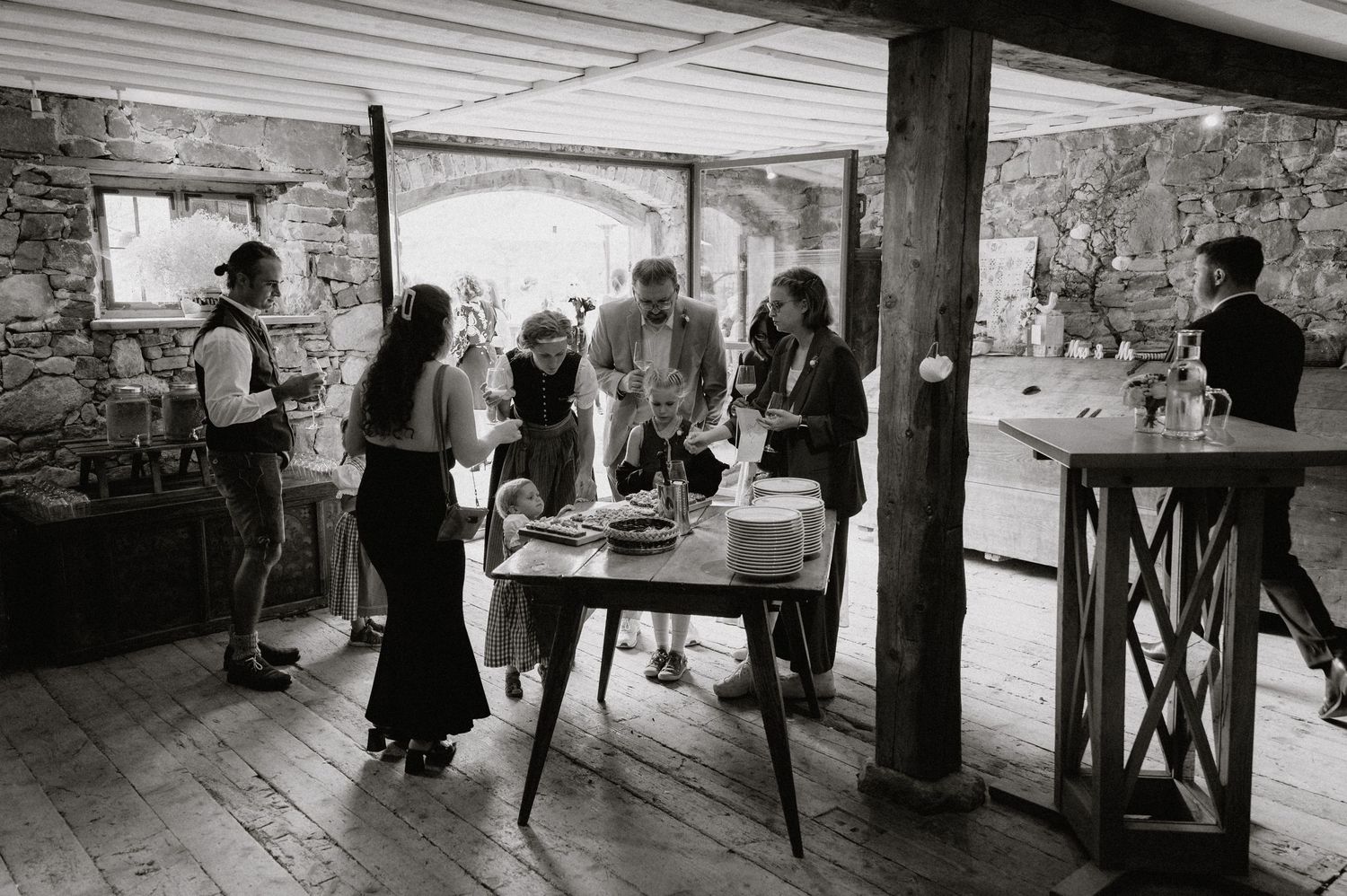 Wedding reception guests mingling around a table in a rustic stone-walled venue.