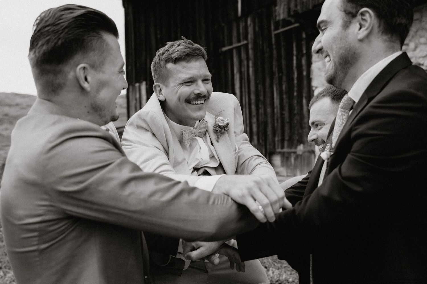 Three men sharing a jovial handshake and laugh outside a barn in vintage black and white photography.