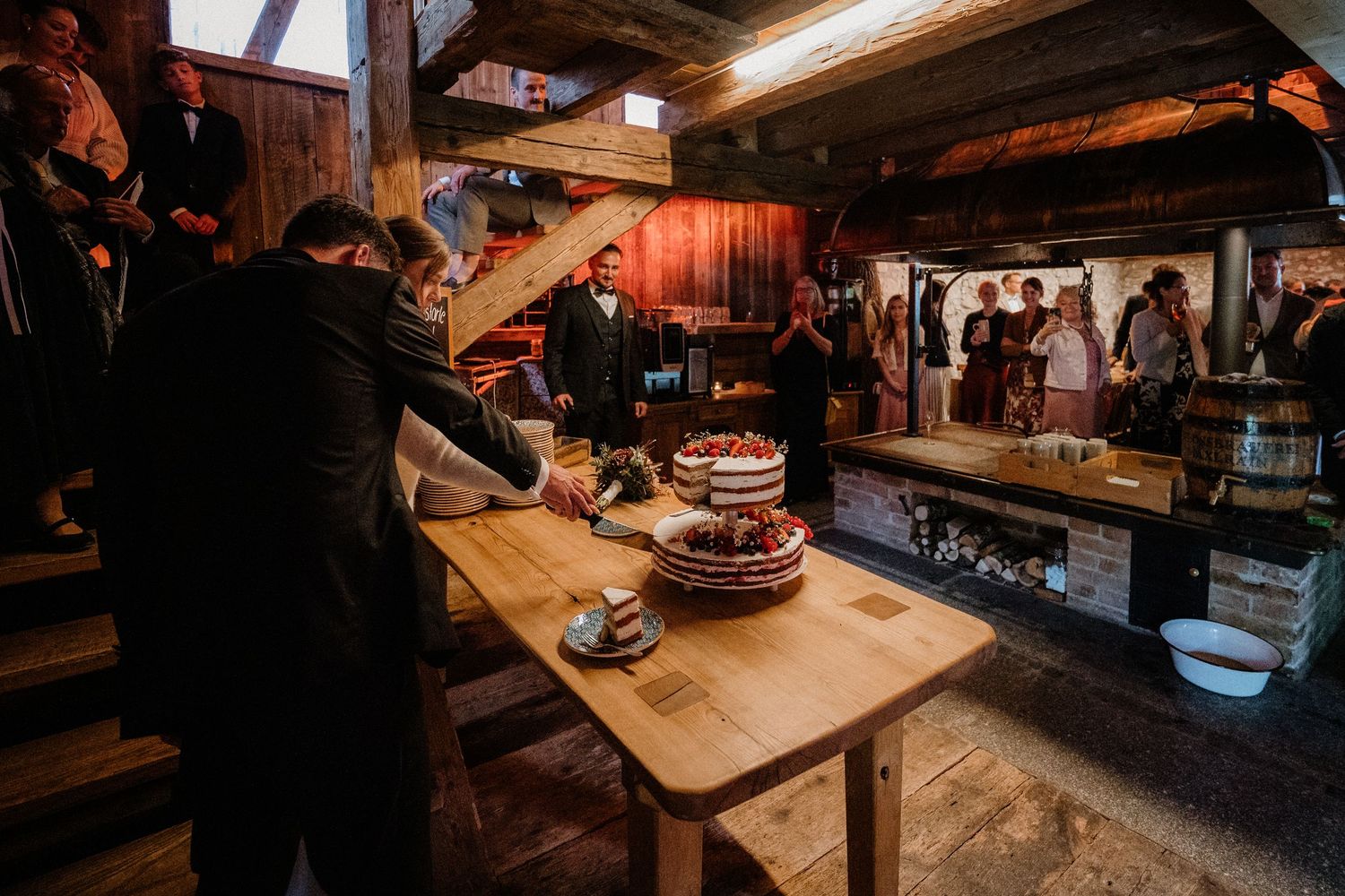 Rustic barn reception with wooden tables and warm lighting creating cozy ambiance.