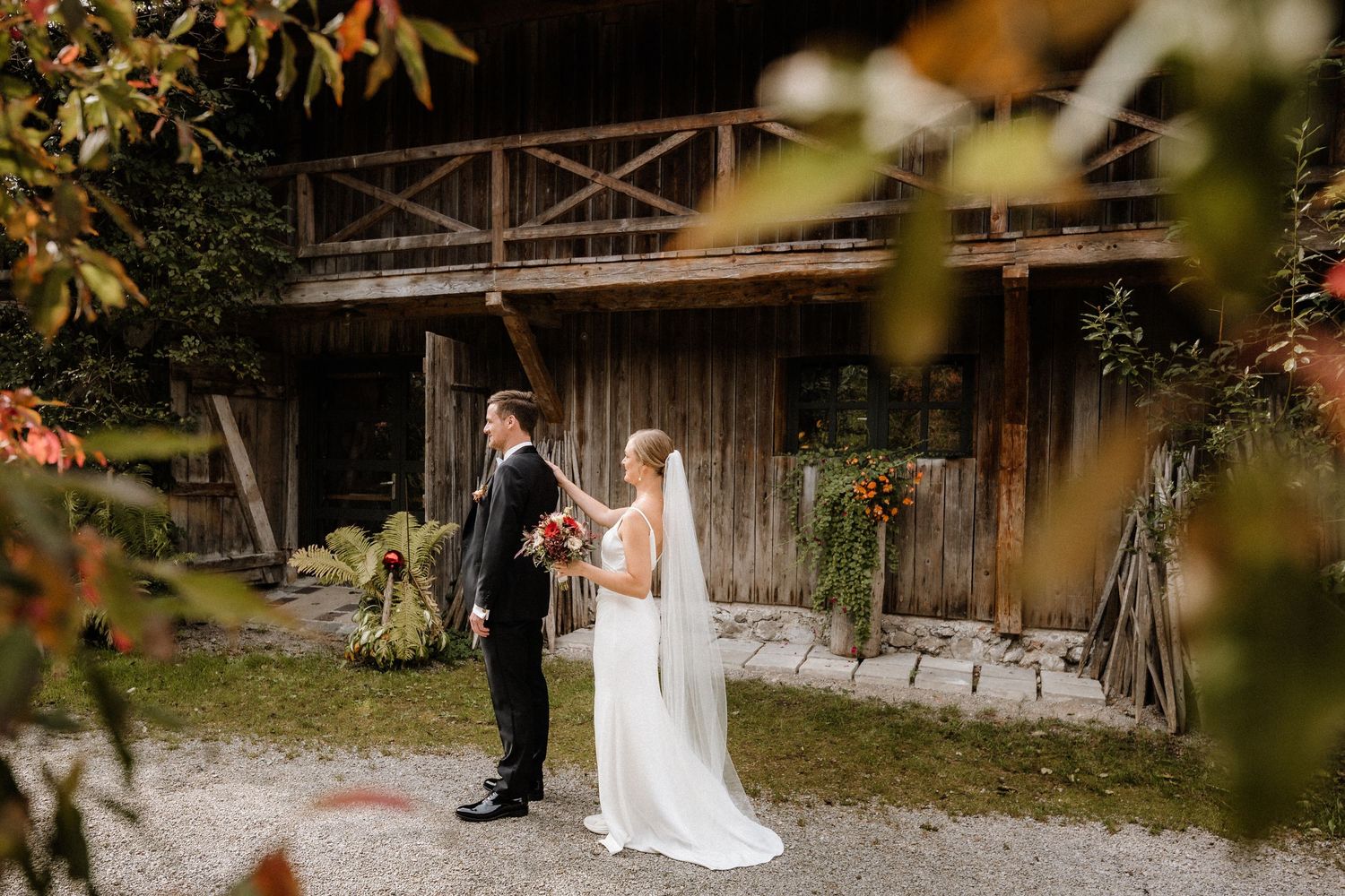 Wedding couple standing in front of rustic wooden barn during autumn.